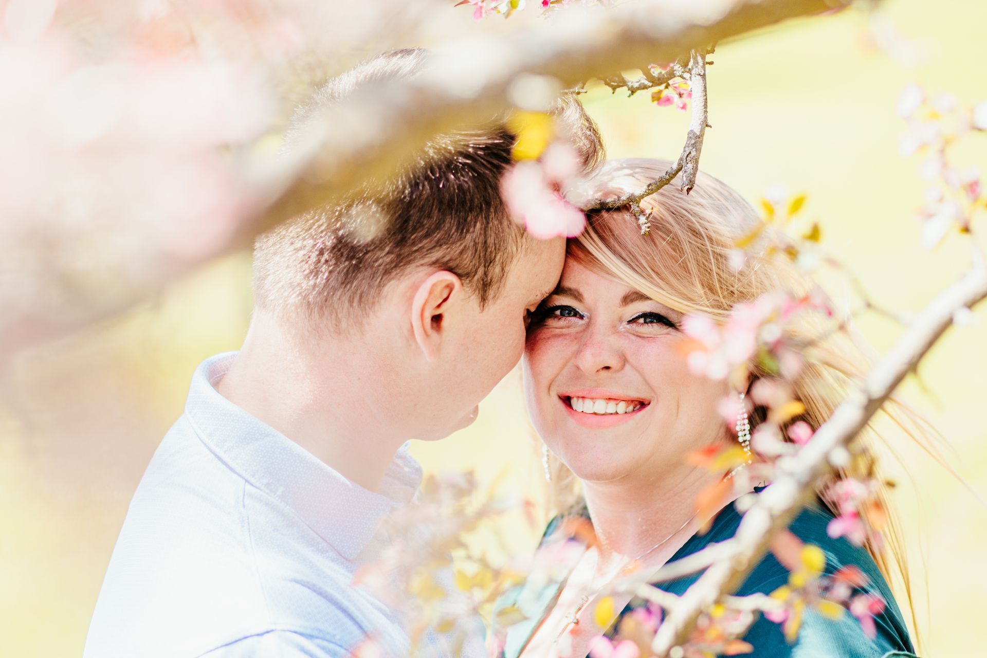 Smiling couple sharing a tender moment among soft pink blossoms outdoors