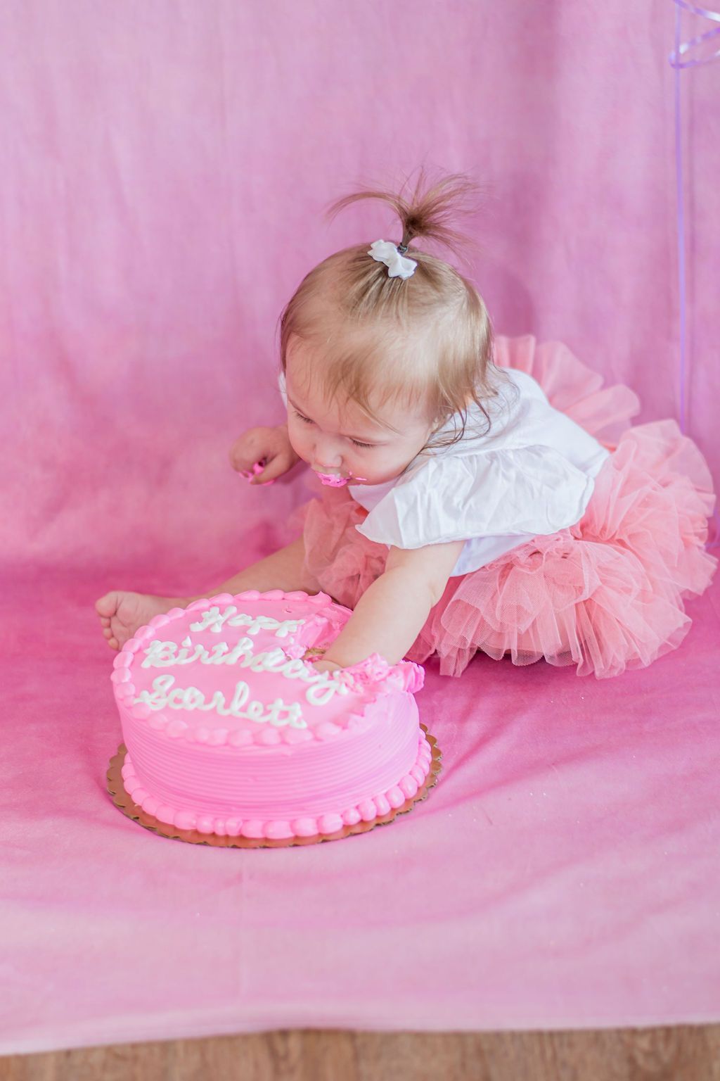 Toddler reaching for a pink birthday cake on a pink backdrop
