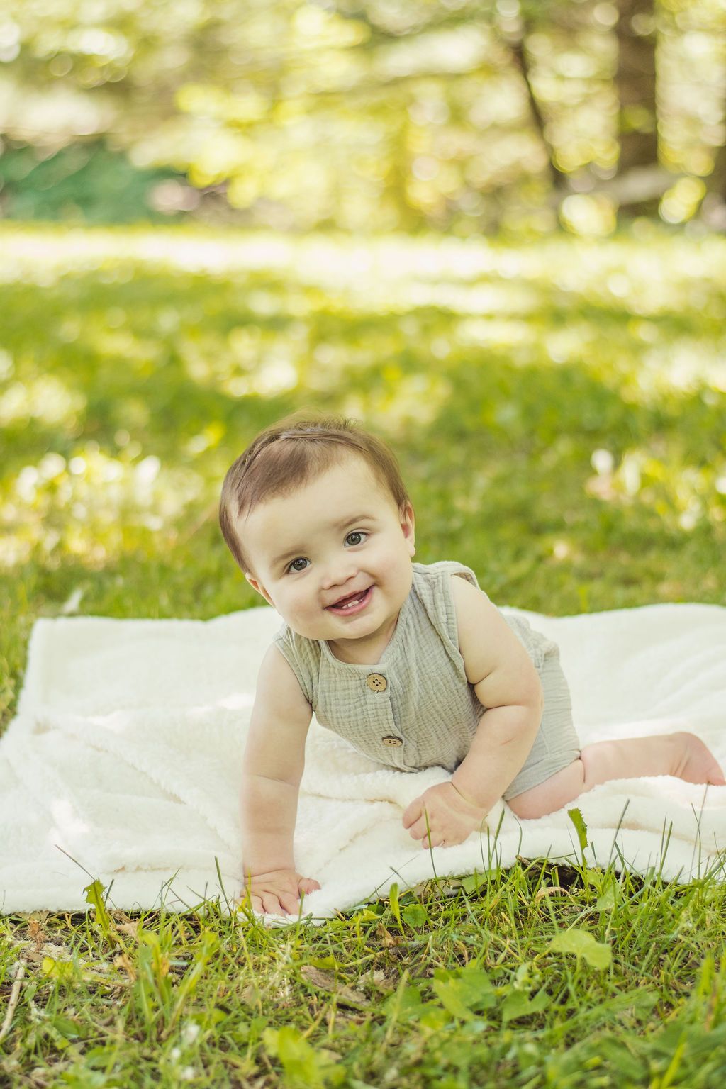 Baby smiling and crawling on a white blanket in a sunlit grassy park