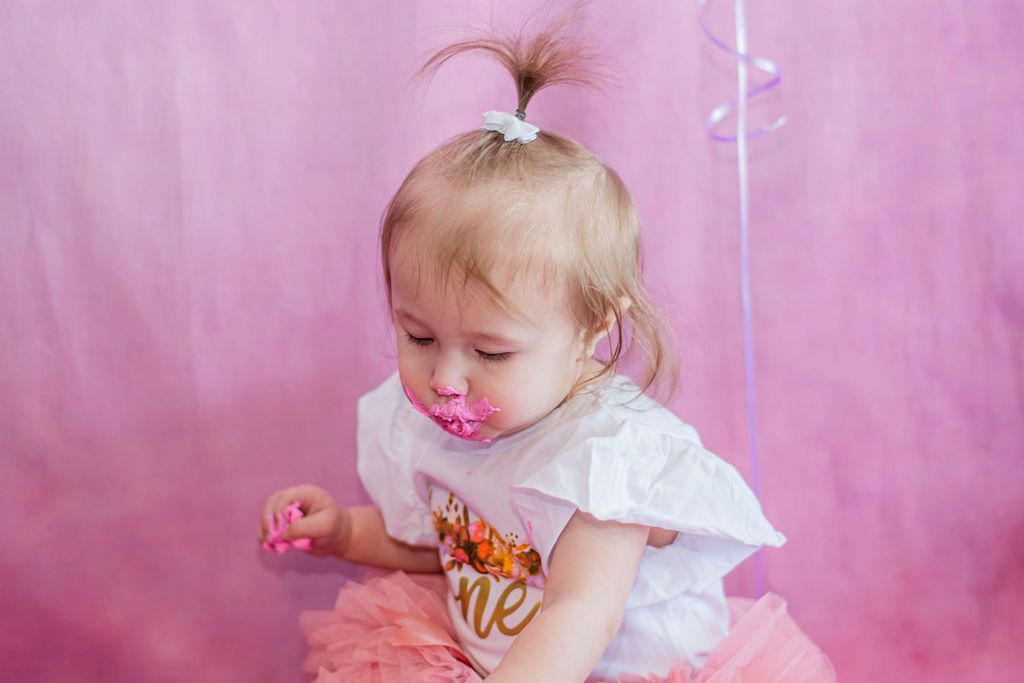 Toddler with pacifier in a white shirt and pink tutu against a pink backdrop