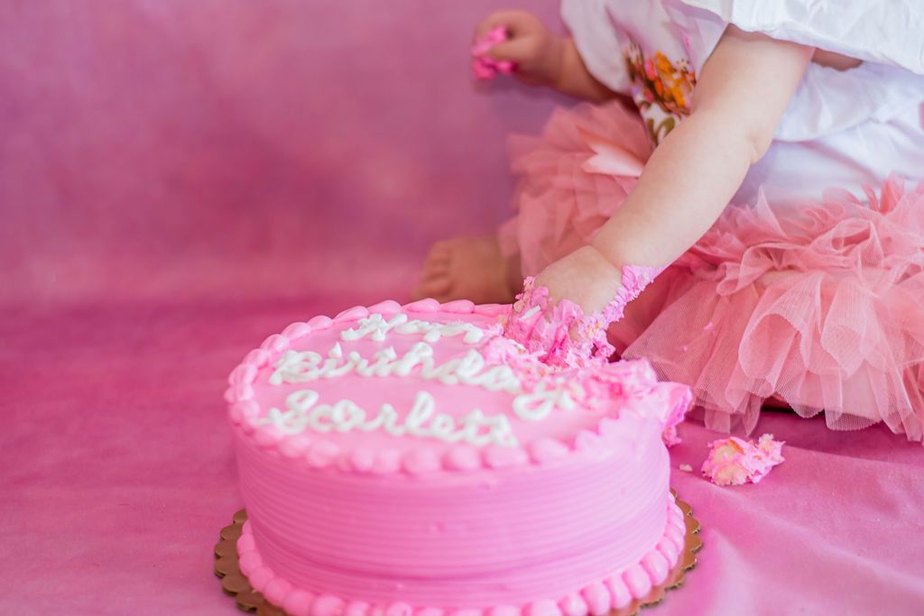 Child reaching for pink frosted cake on pink table with pastel decorations