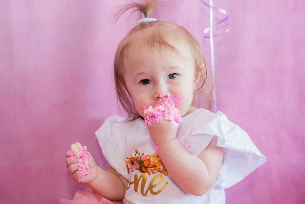 Toddler holding and eating pink frosted cupcakes against a pink backdrop