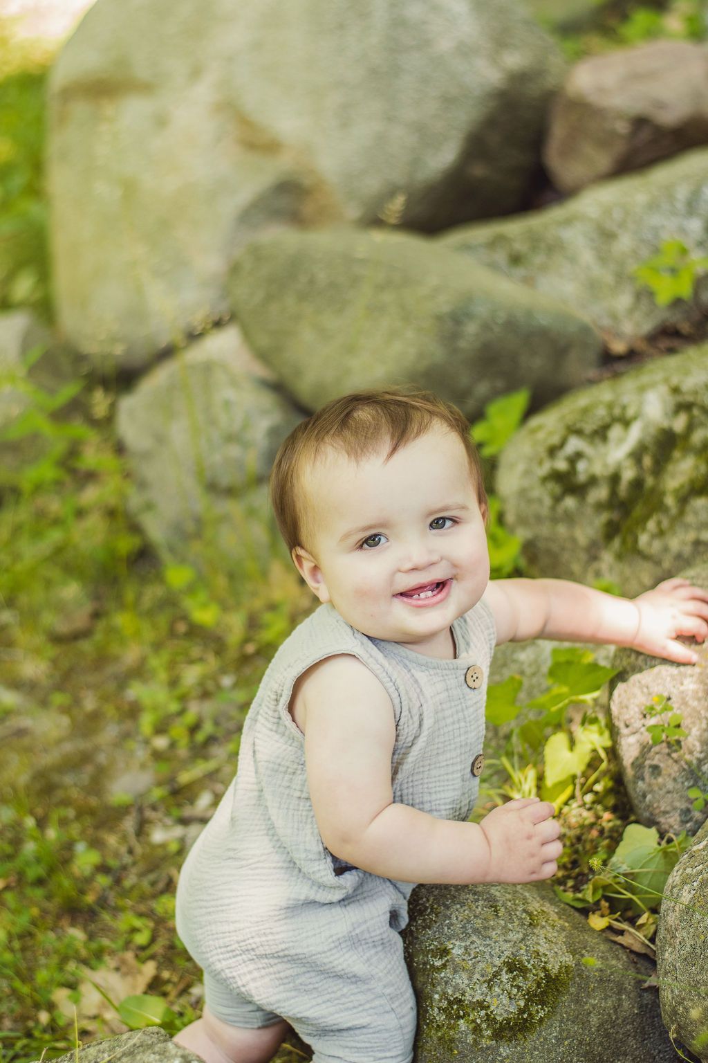 Smiling child in a gray romper climbing mossy rocks outdoors