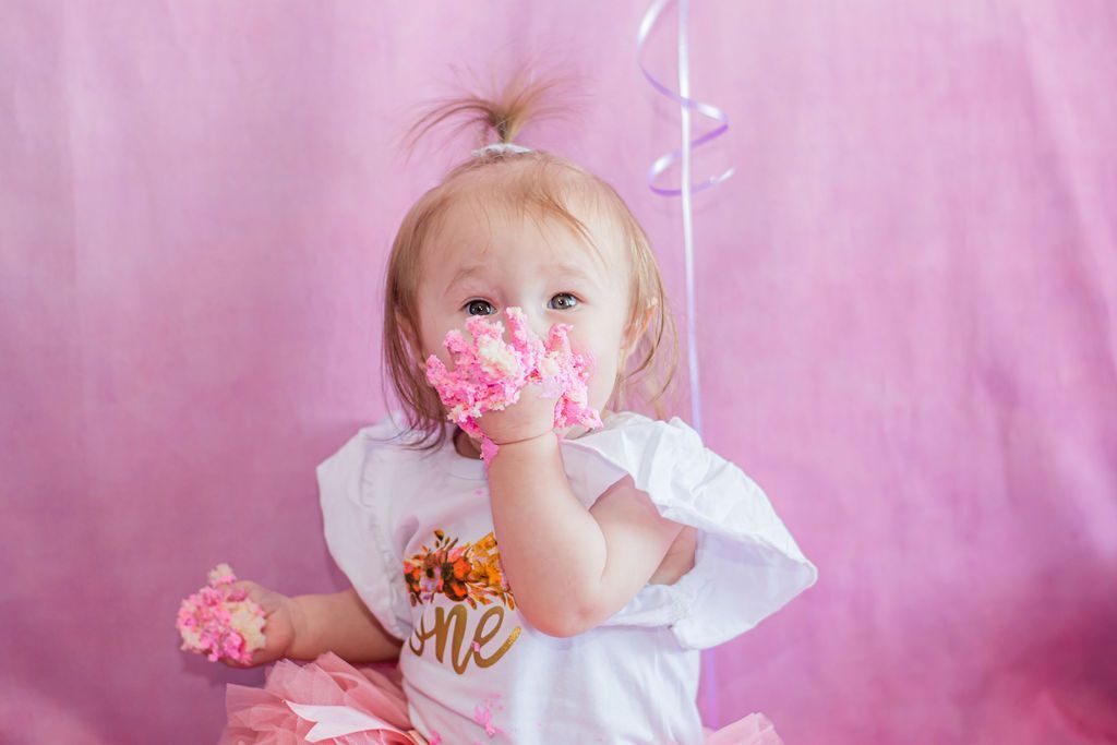 Young child holding pink flowers in front of a pink backdrop, wearing a white shirt.