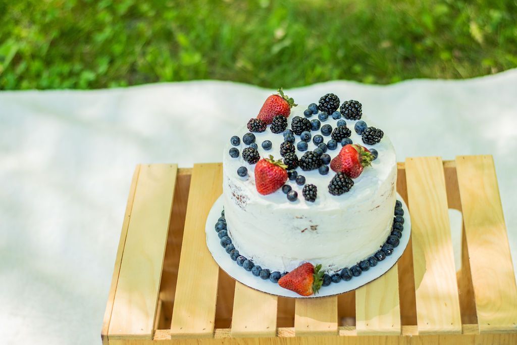 Small white frosted cake topped with berries on a wooden slat table outdoors