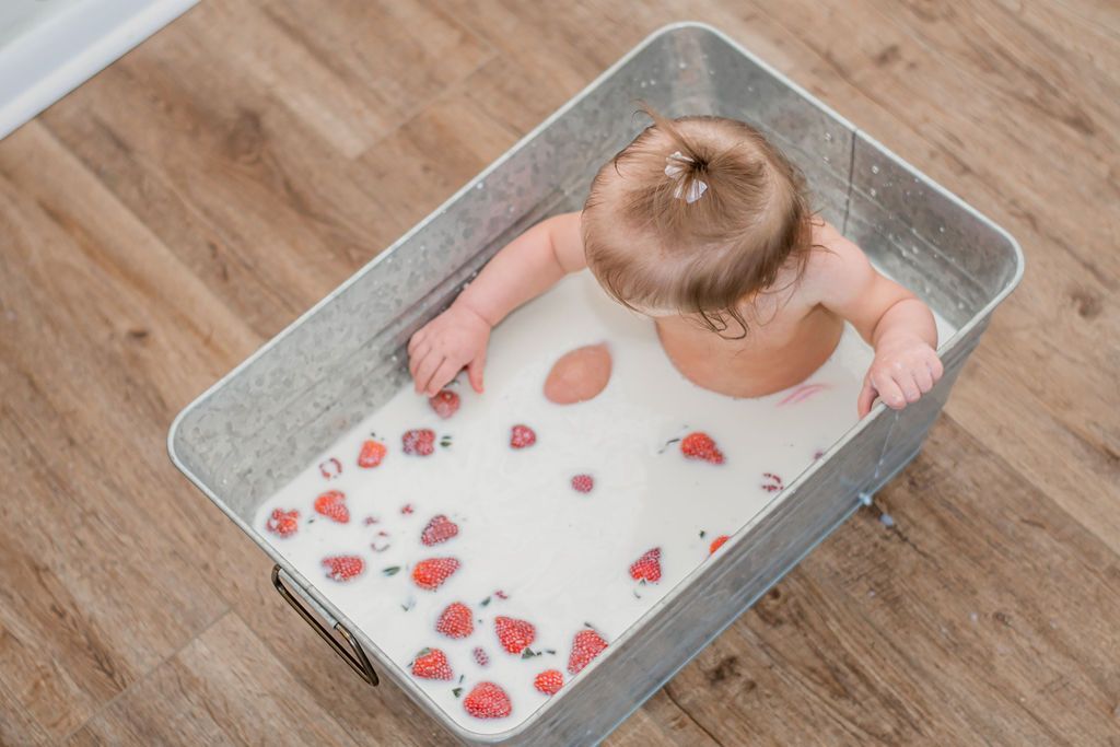 Baby in a metal tub of milky water with strawberries, viewed from above