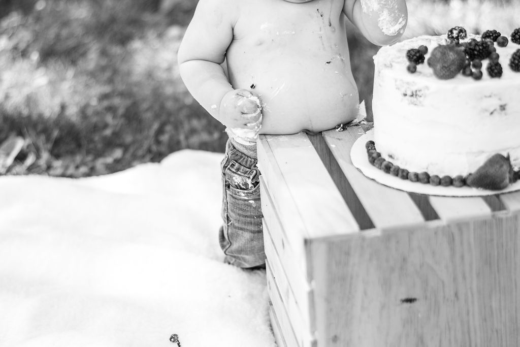 Child standing by a cake outdoors in the snow