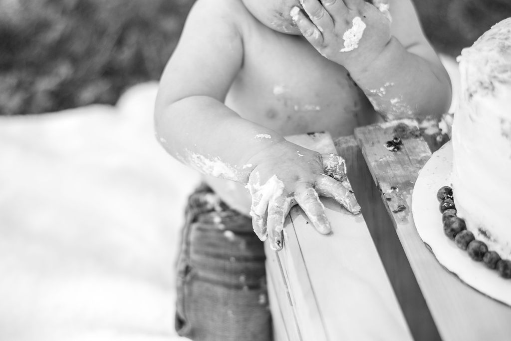 Baby with frosting-covered hands touching a cake at a party