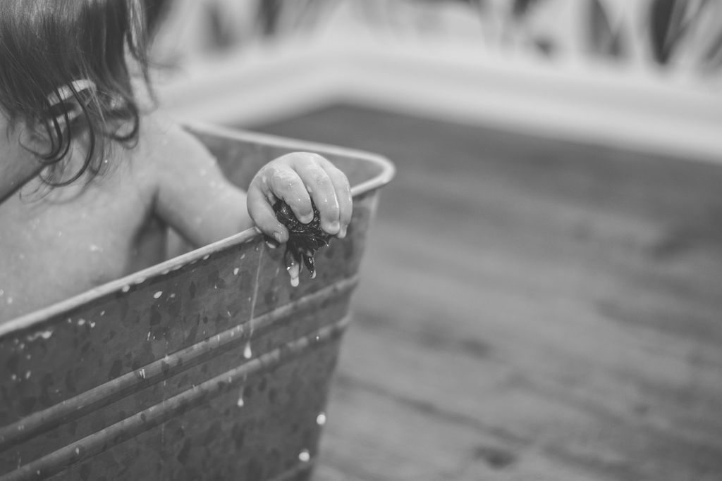 Child peeking from a metal tub, hand on the rim, in a black-and-white indoor scene.