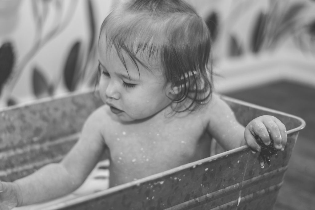 Child standing in a wooden tub, looking down with one hand on the rim.