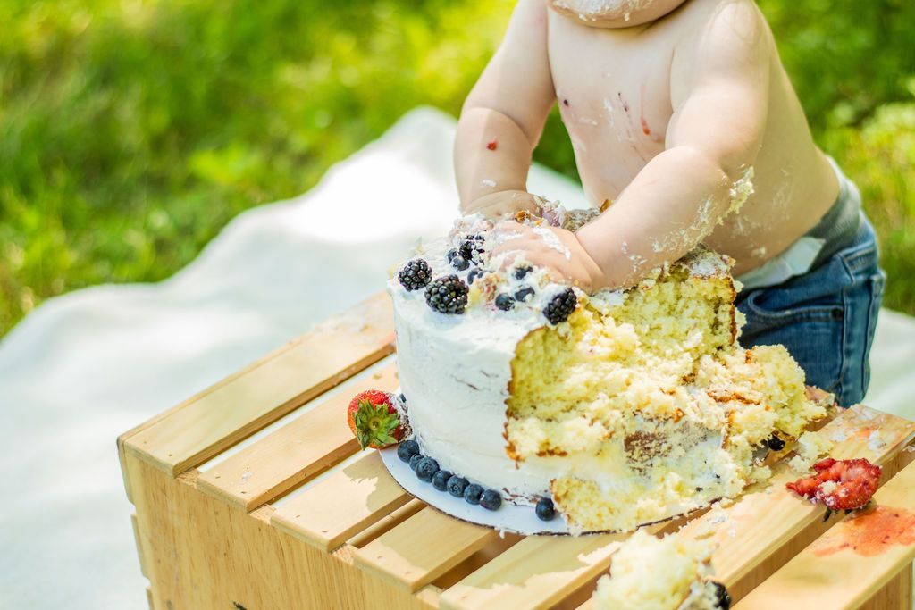 Child smashing a white frosted cake on a wooden crate outdoors in the grass