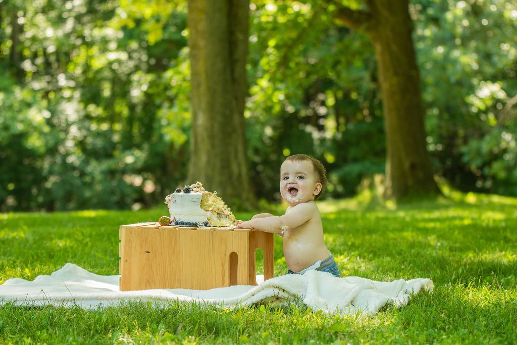 Baby splashing in a white blanket beside a wooden tub outdoors in a sunny green park