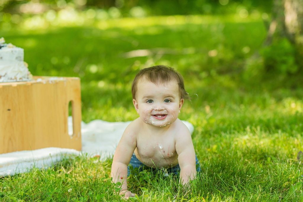 Baby crawling on grass outdoors near a wooden box, smiling in a sunny green yard