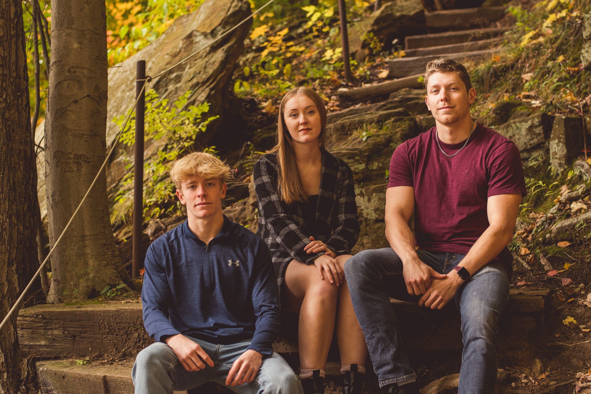 Three people sitting on outdoor steps beside trees and autumn foliage