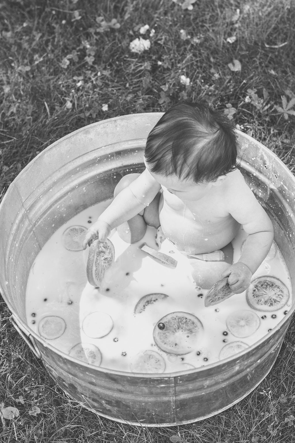 Child sitting in a small inflatable pool, playing with water and toys outdoors.