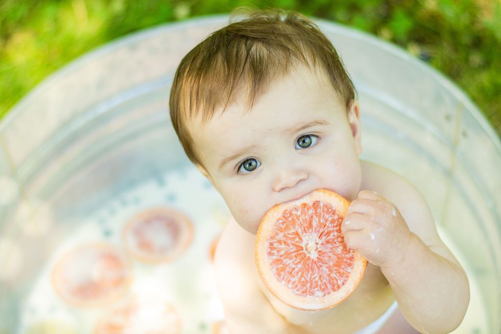 Child in a tub eating a grapefruit half, with a soft green and blue background
