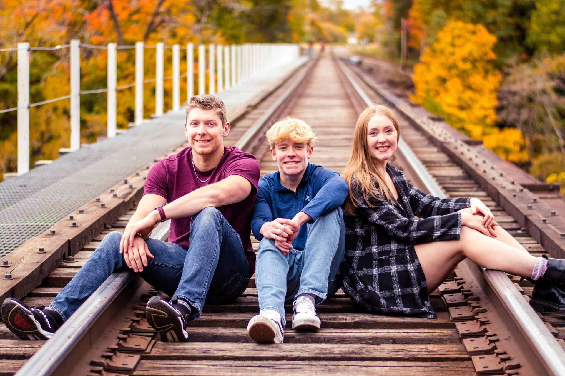 Three friends sitting on railroad tracks in autumn, smiling at the camera