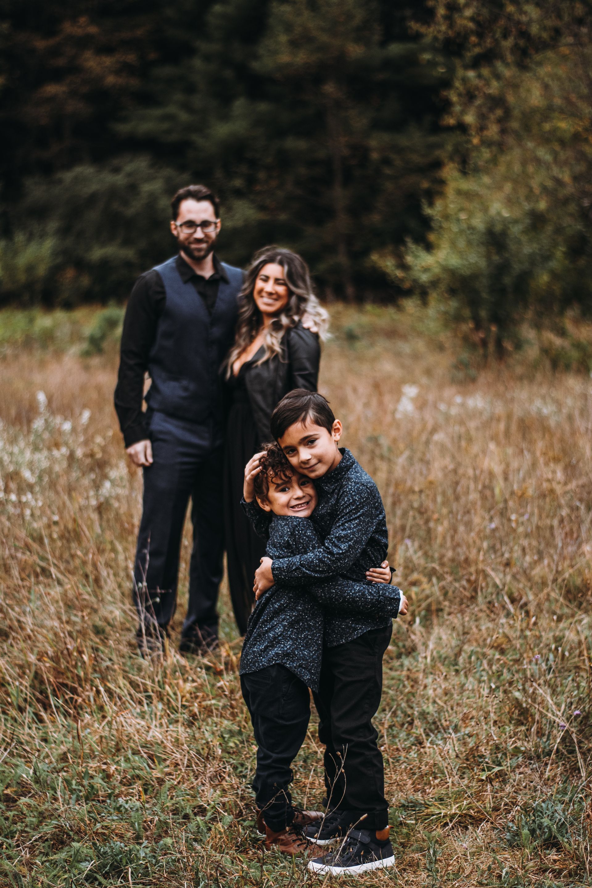Three people hugging in a grassy field, with a dark forest backdrop.