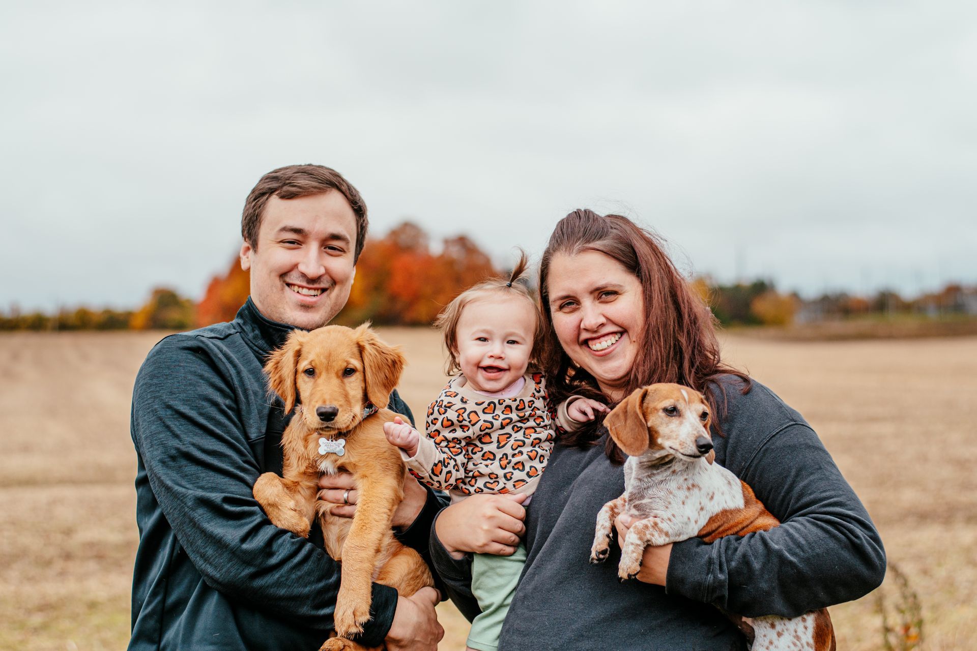 Family sitting outdoors in a field with two dogs, smiling at the camera