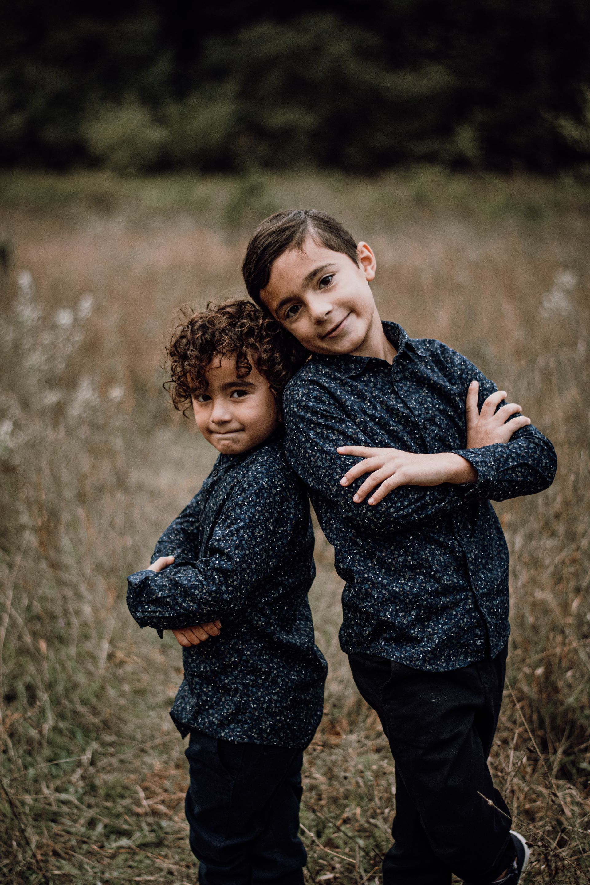 Two children in matching dark shirts standing together in a grassy field, smiling at the camera