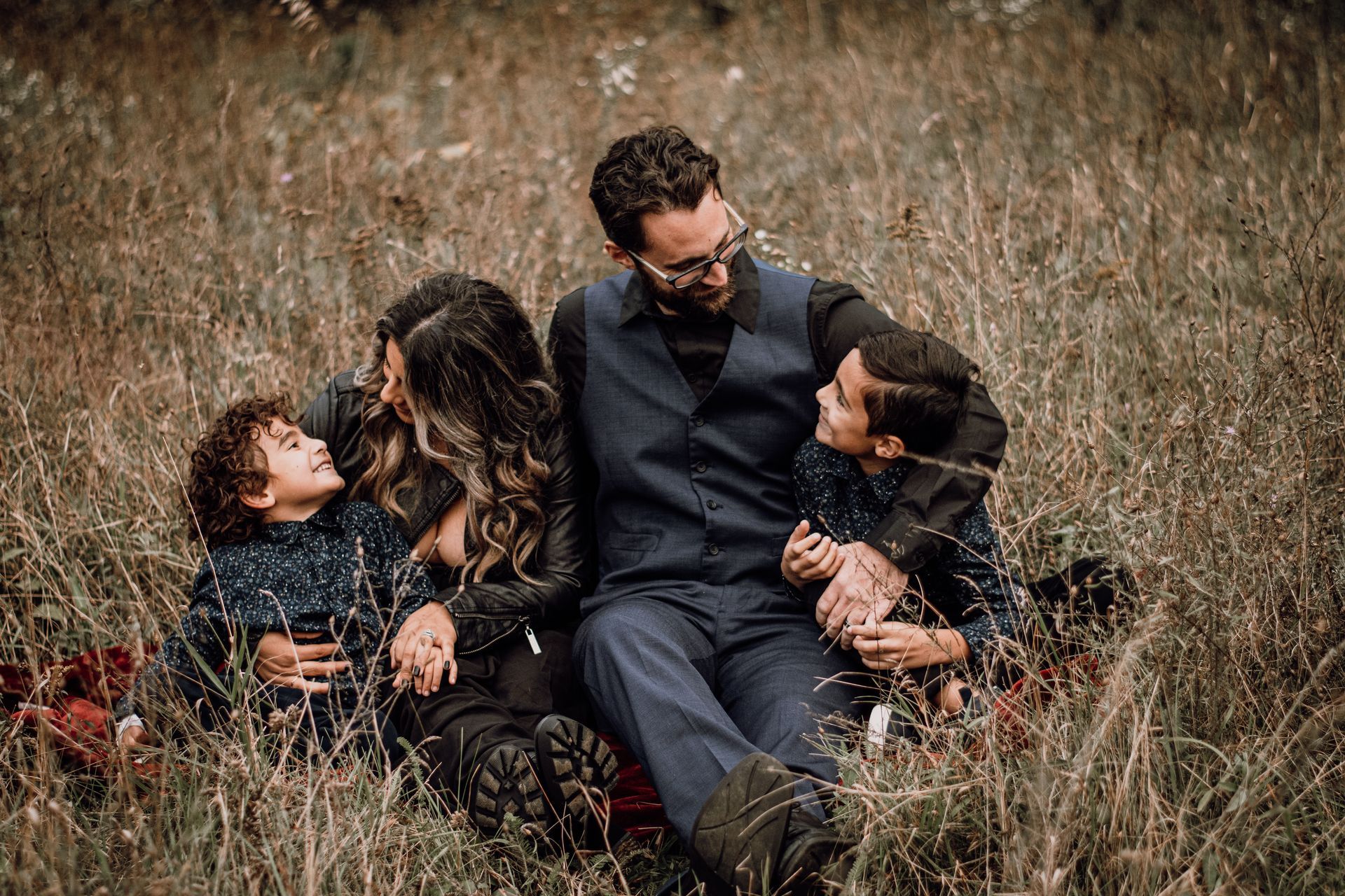 Family sitting together in tall grass, smiling and talking in a warm outdoor setting