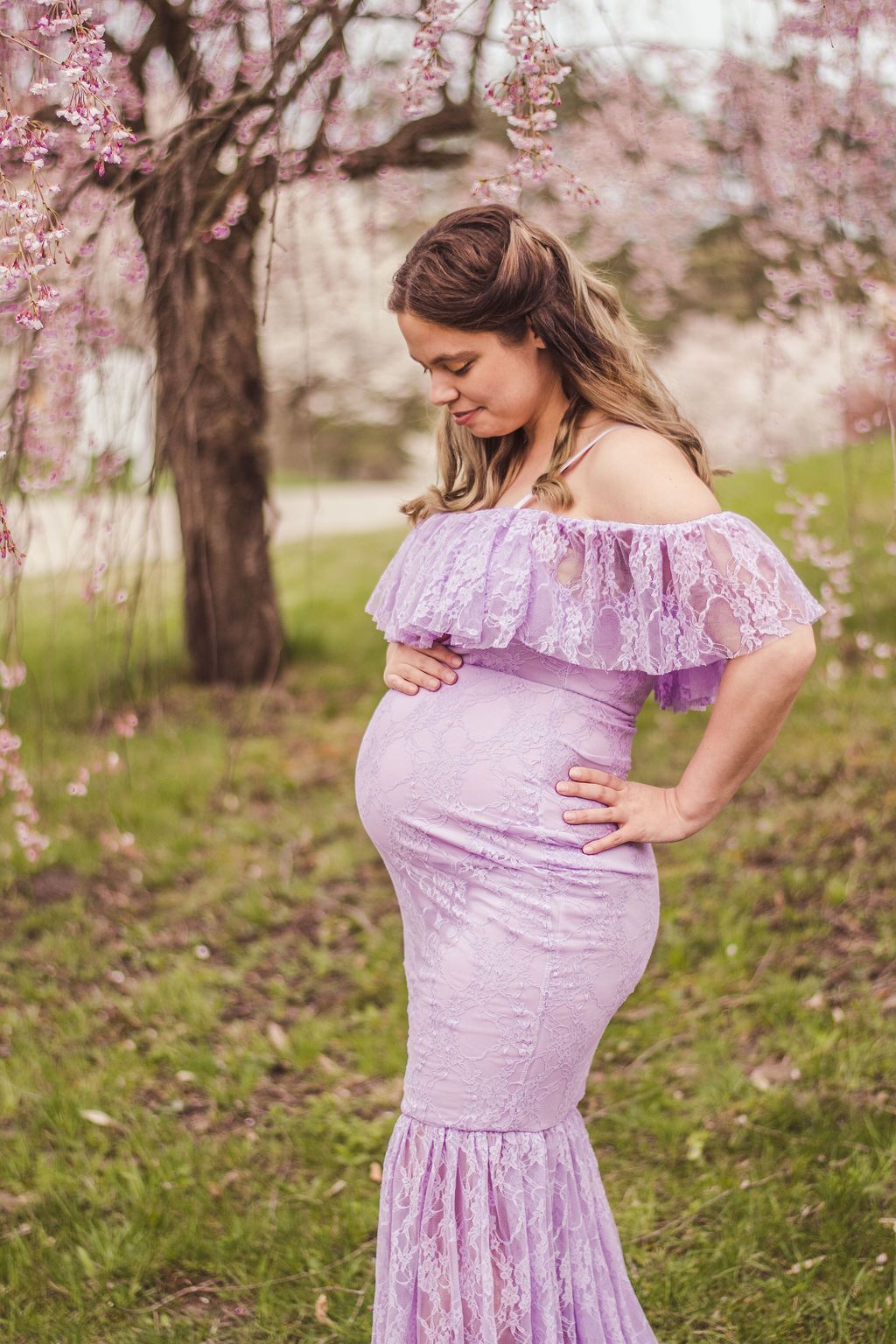 Pregnant woman in a lavender dress posing in a blooming orchard