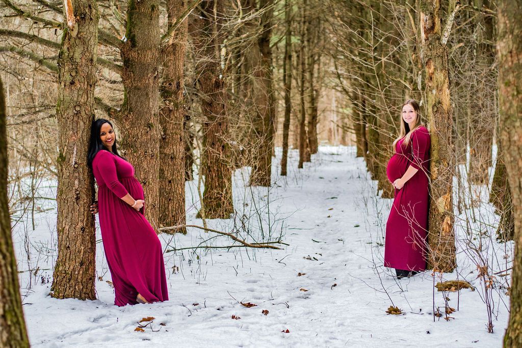 Two women in magenta dresses pose among snowy trees in a winter forest