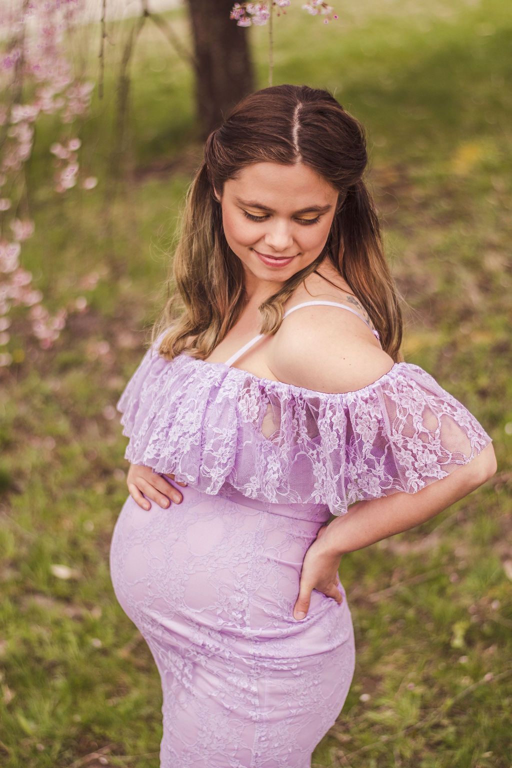 Pregnant woman in a lavender dress posing outdoors with one hand on her belly