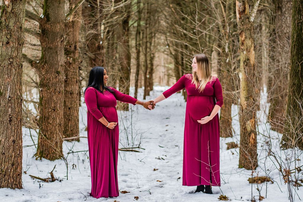 Two people in magenta dresses holding hands in a snowy forest path