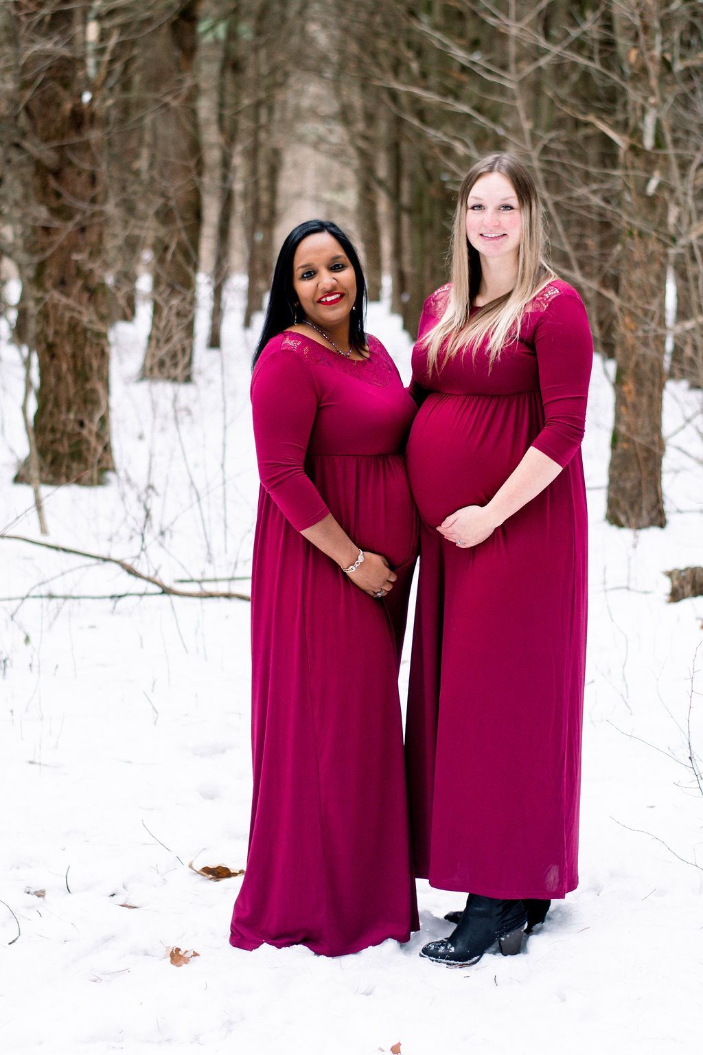 Two women in matching magenta dresses standing together in a snowy wooded area