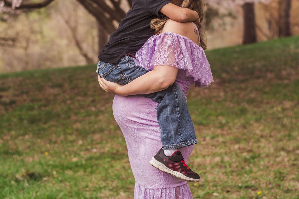 Person carrying a child outdoors in a grassy park, both in purple clothing