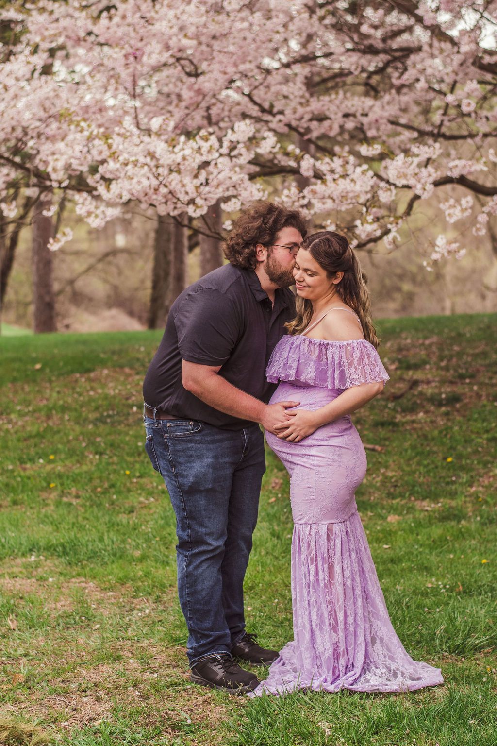 Couple embracing under blooming cherry trees in a park, with the woman in a lavender dress