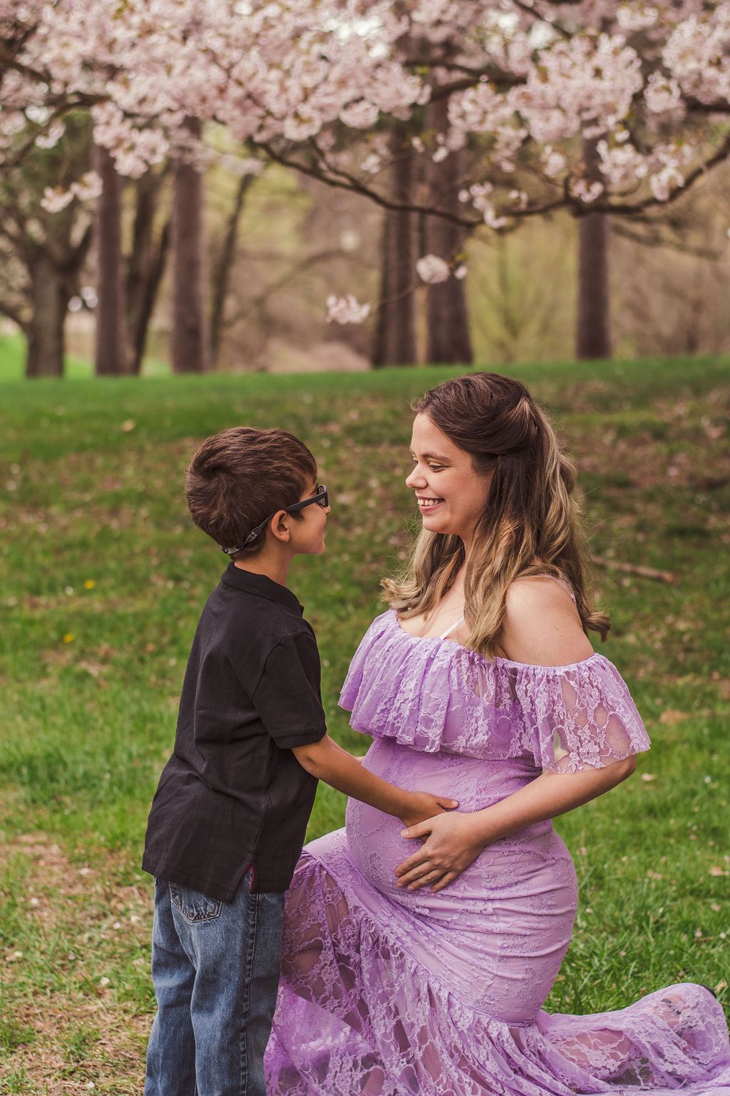 Two people holding hands in a park, one in a lavender dress with blooming cherry trees behind them.