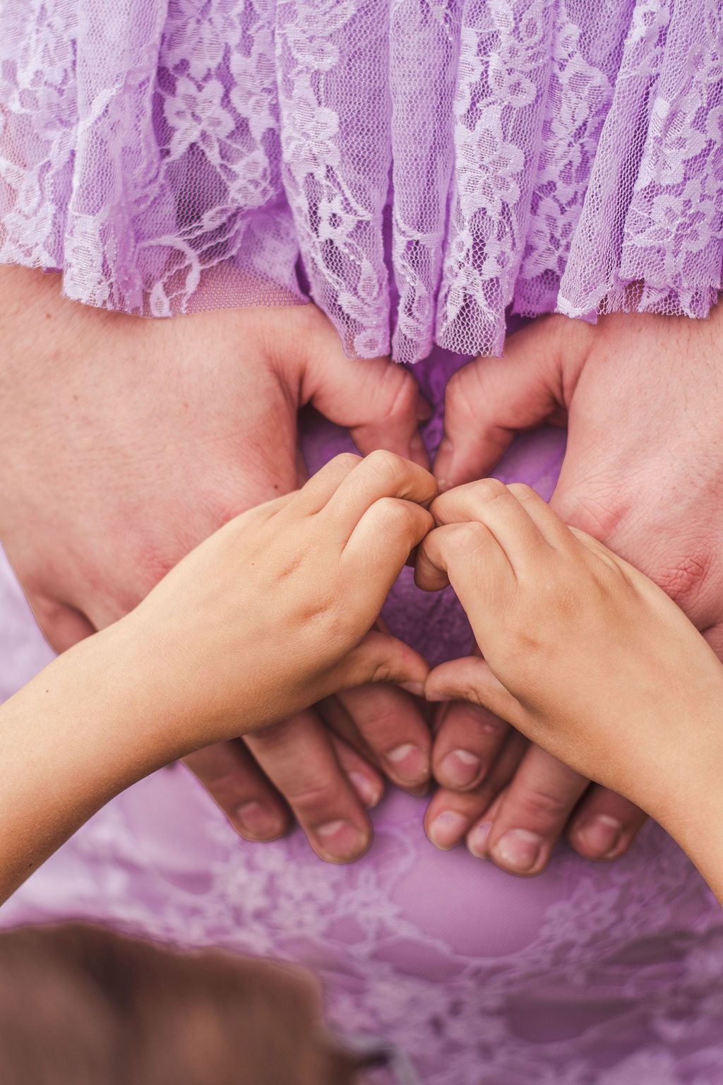 Hands of different sizes forming a heart over a purple lace dress.