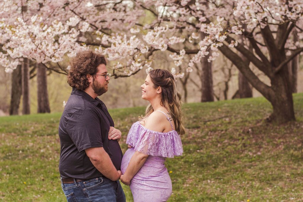Couple holding hands under blooming cherry trees in a park, smiling at each other.