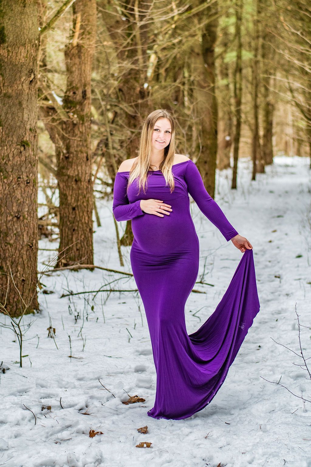 Woman in a purple dress standing in a snowy forest and holding the gown’s train