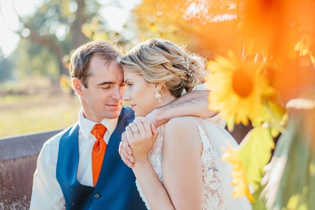 Couple embracing outdoors, with orange flowers in the foreground and warm sunlight.