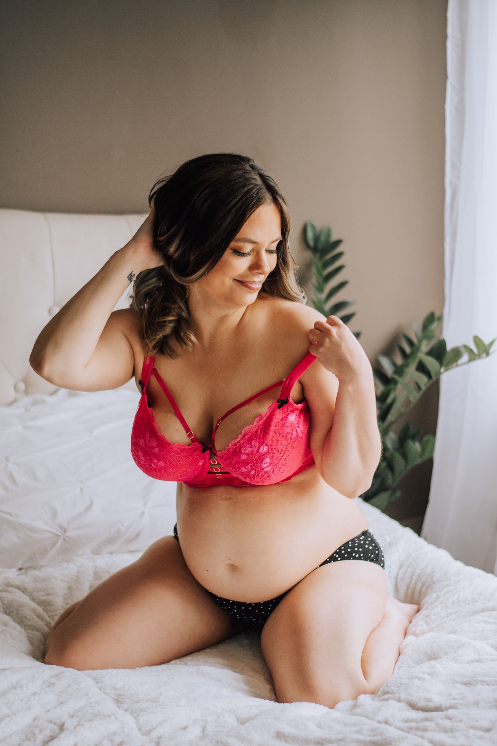 Woman sitting on a bed in pink lingerie, looking down with one hand in her hair.