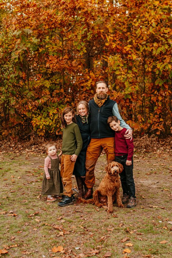 Family with two children and a dog standing in autumn leaves before orange foliage