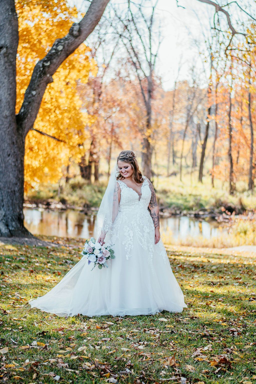 Bride in a white gown holding a bouquet in an autumn park by a pond