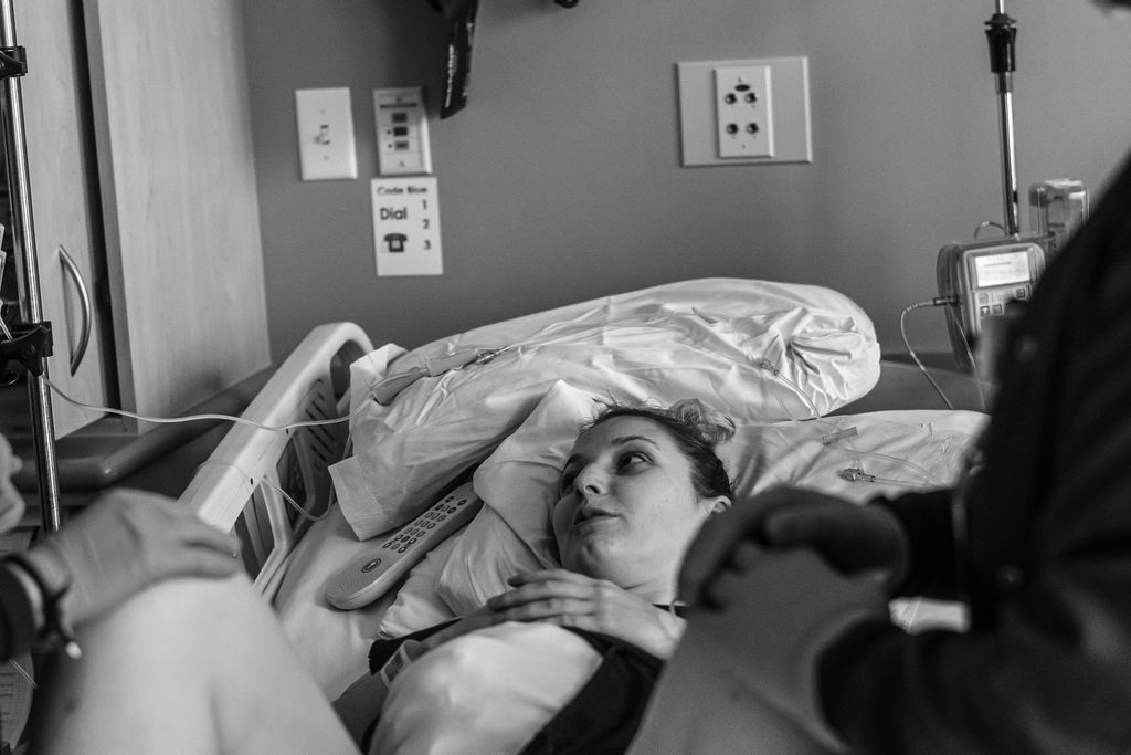 Patient lying in a hospital bed, looking up while a caregiver stands nearby