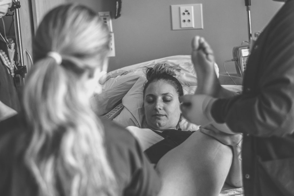 Woman in a hospital bed while staff stand nearby, one holding a newborn.