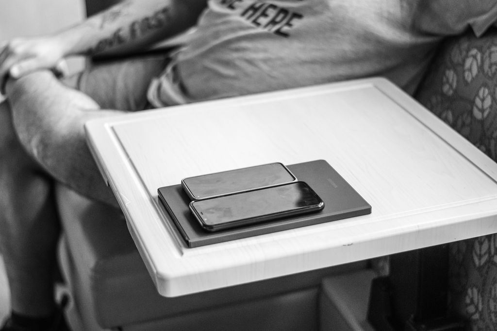 White tray table with a small rectangular device beside a resting person's arm in black and white.