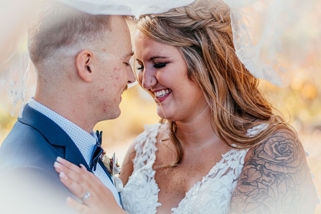 Bride and groom smiling forehead to forehead in a warm outdoor wedding portrait
