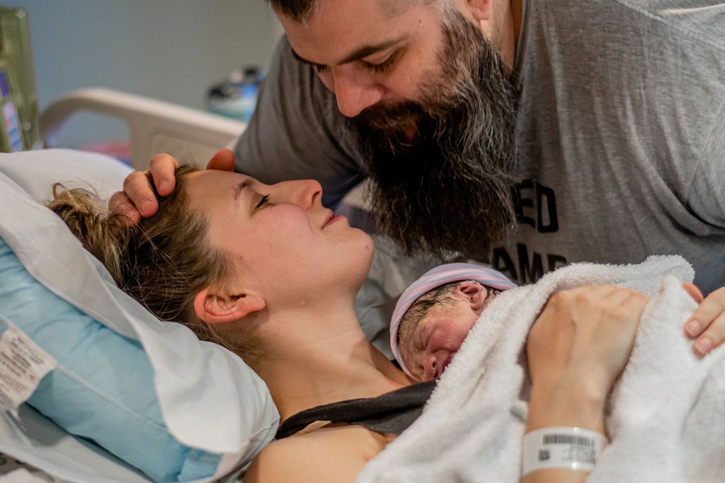 Man comforting partner in hospital bed holding newborn baby