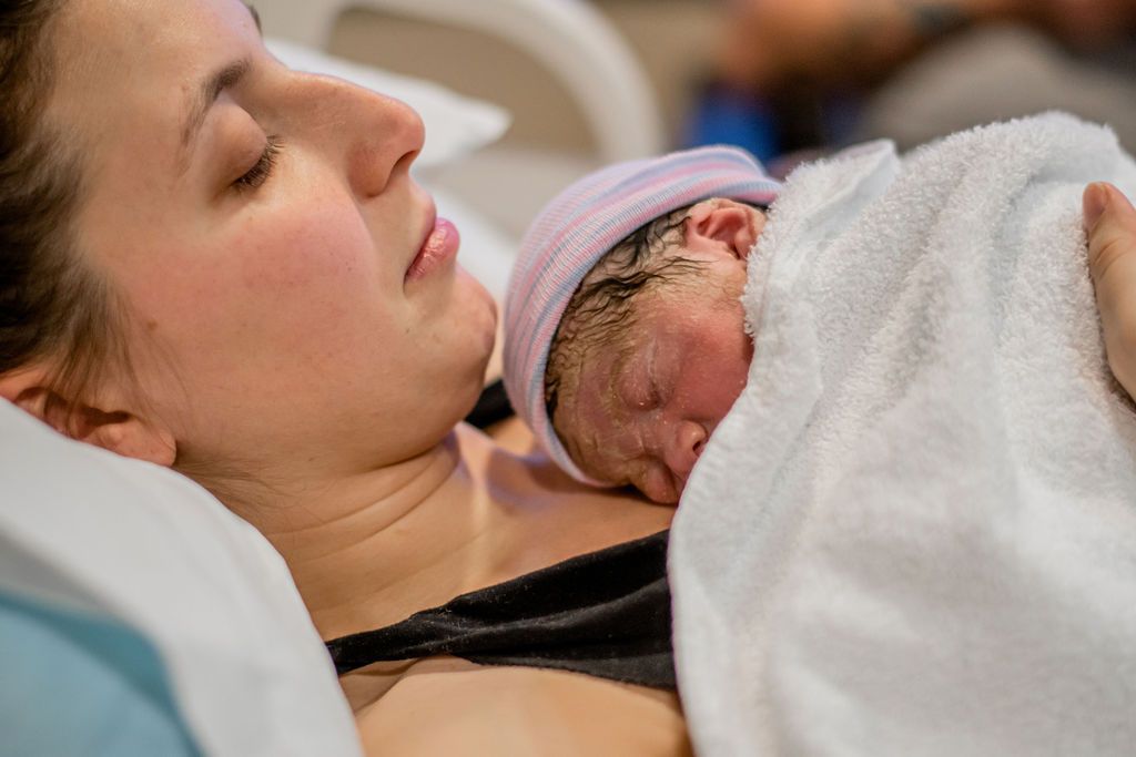 Mother holding sleeping newborn wrapped in a white blanket in a hospital bed