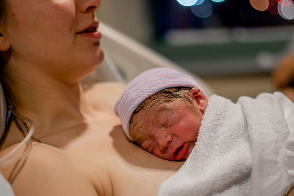 Newborn baby wrapped in a white blanket, resting against a woman’s chest