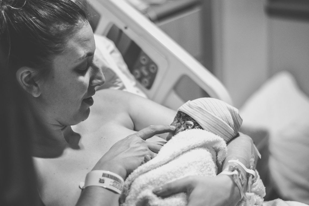 A parent holding a newborn in a hospital bed, with a woman leaning close beside them.