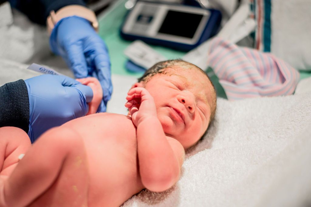 Newborn being weighed and cleaned by gloved medical staff in a hospital delivery room