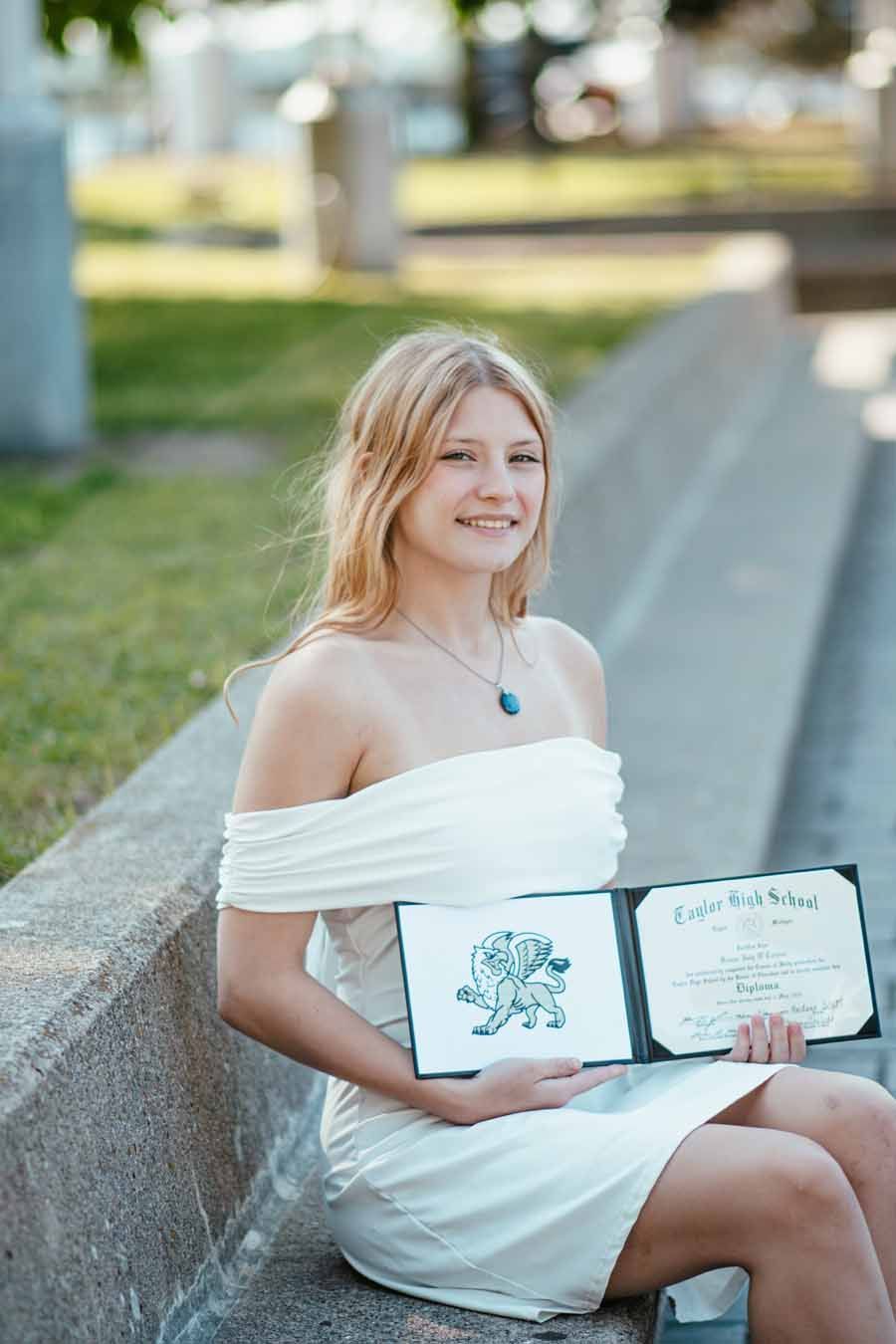 Woman in a white dress sitting outdoors, smiling and holding an open photo album.